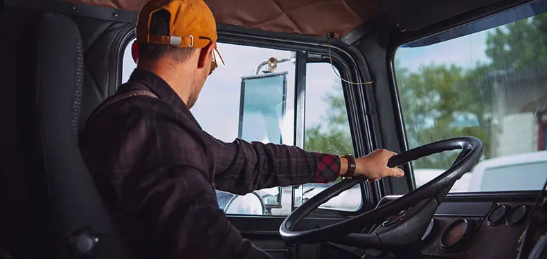 A photo of a truck driver looking out his driver side window while behind the steering wheel of their truck.