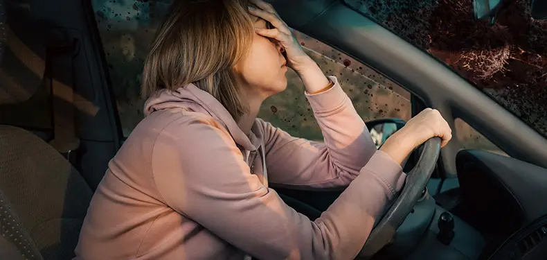A photo of a woman behind her steering wheel holding her face after an accident.